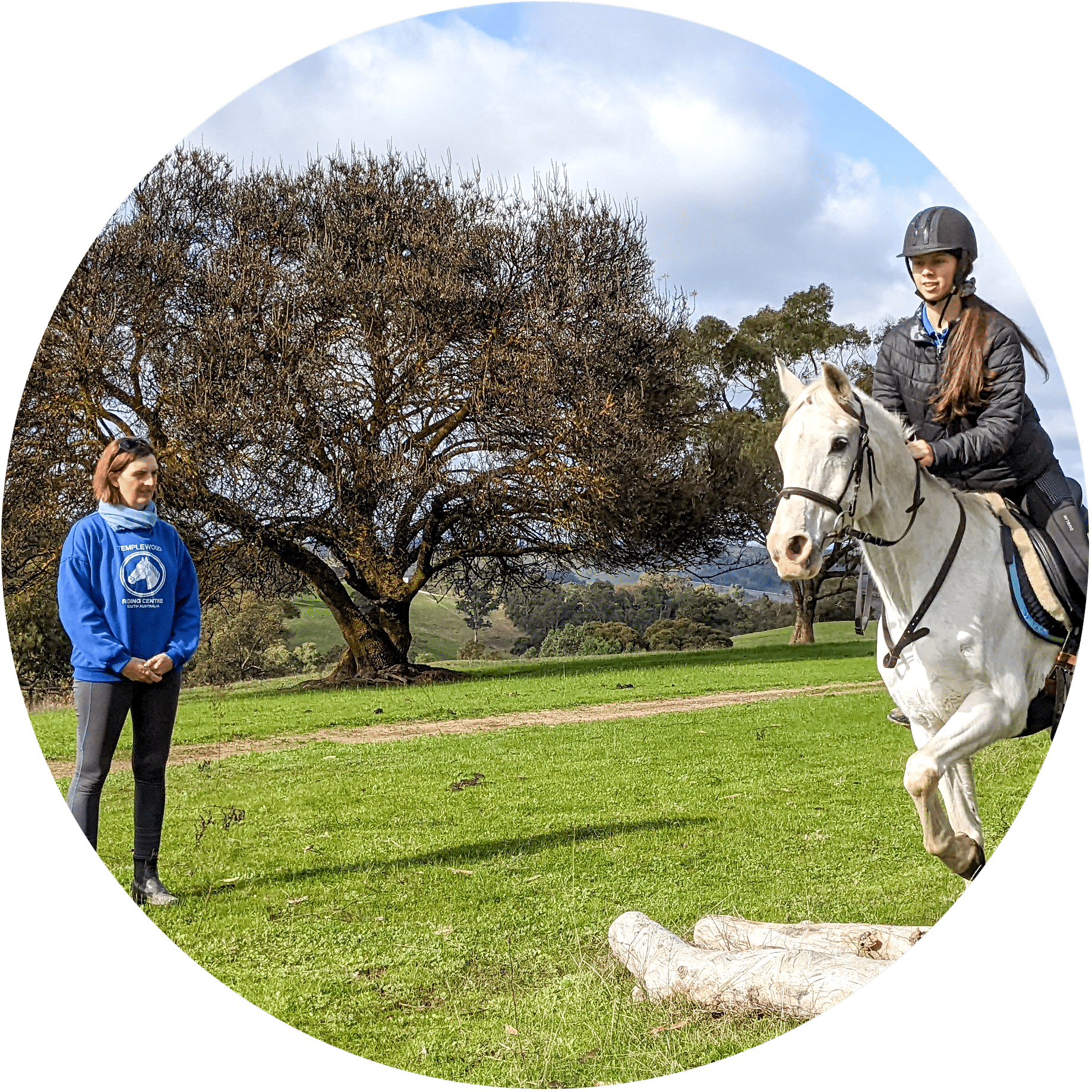 crosscountry-circle a riding instructor in a templewood jumper watches while a woman jumps her horse over a small log