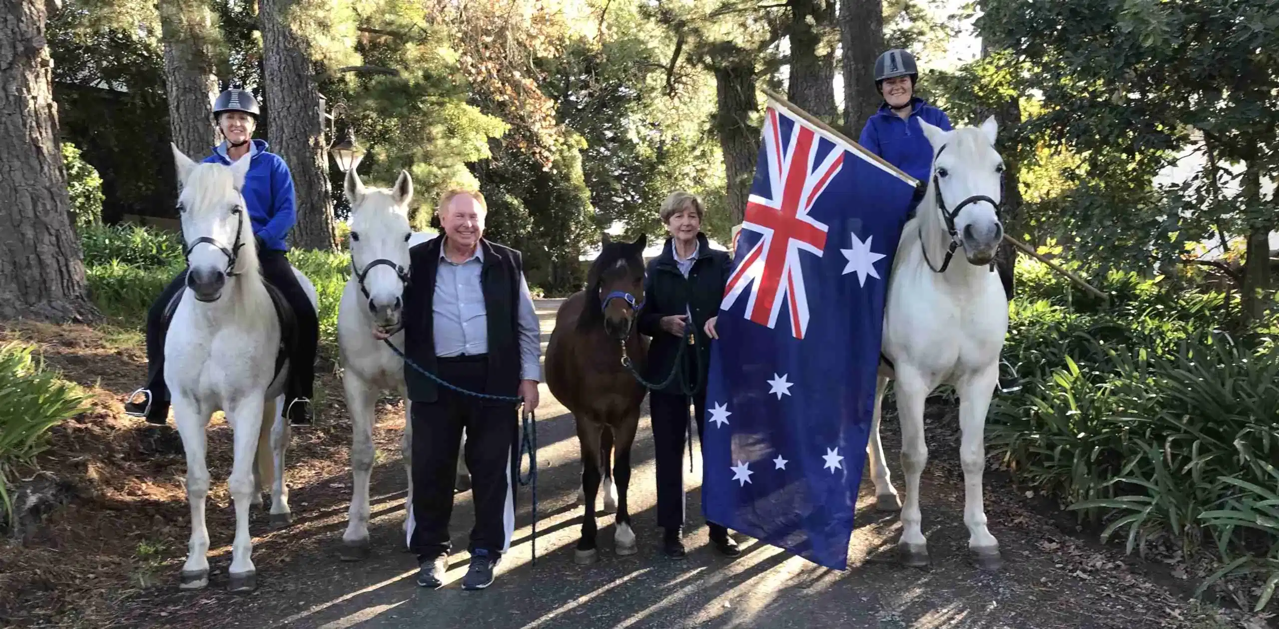 flag-horses several adults and horses pose on a bush track. one rider holds an australian flag