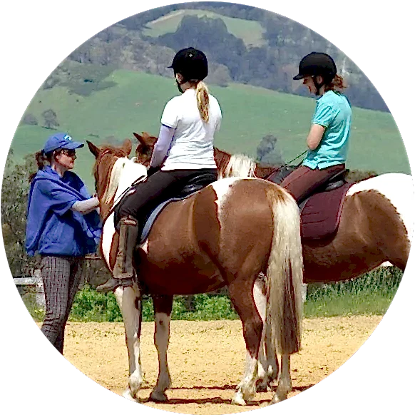 grouplessons-circle two riders sit on their horses in a rural environment while a woman in a templewood shirt stands patting their horses