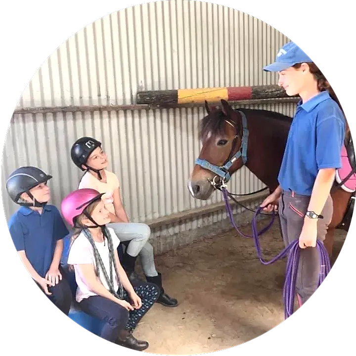 dayschool-circle2 young students at a day riding school sit and look at their instructor, who holds a pony by the reins